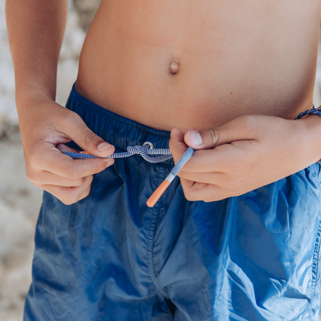 Boy tying the drawstring on Lison Paris Capri swim shorts in blue