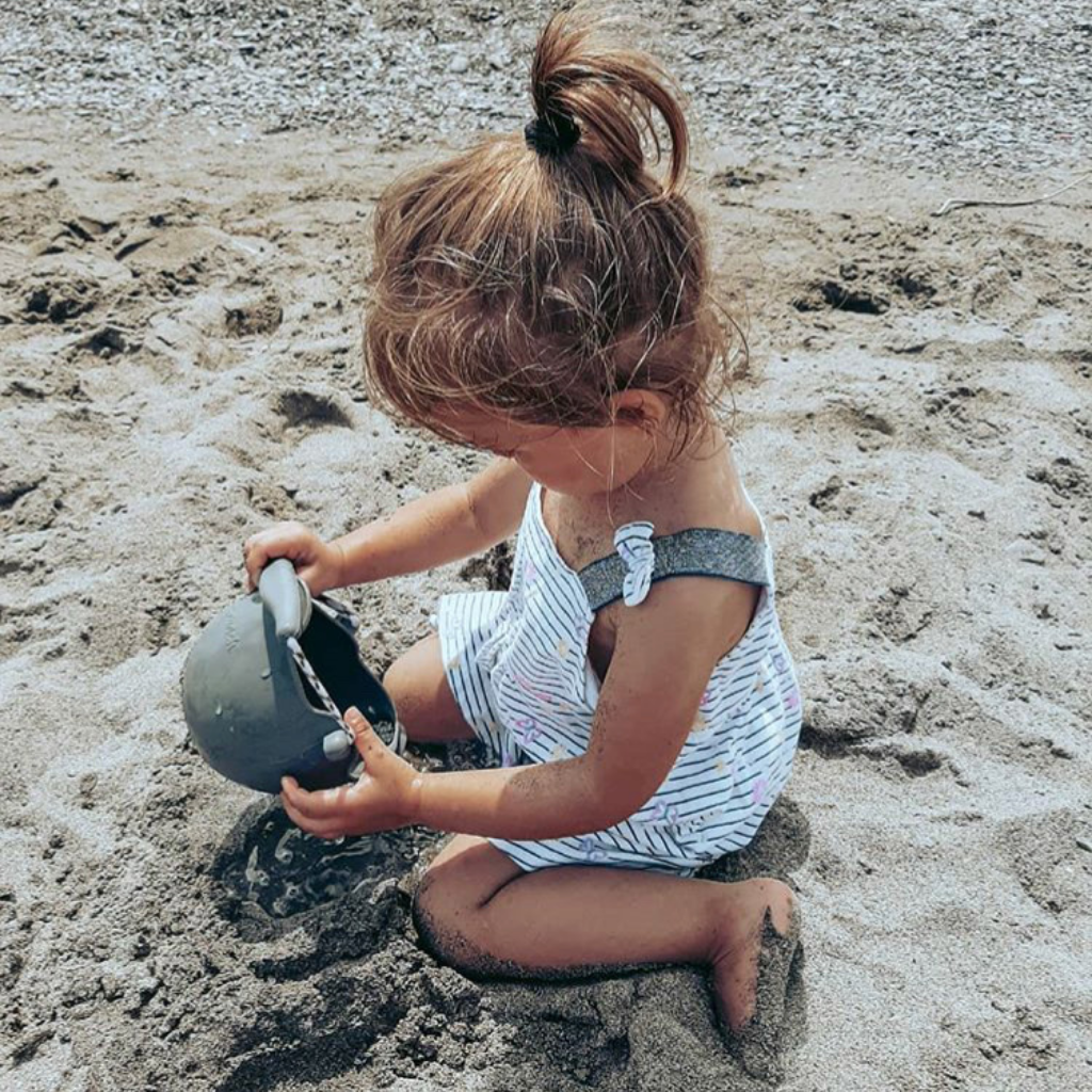 Little girl on the beach playing with her Scrunch silicone watering can in anthracite grey