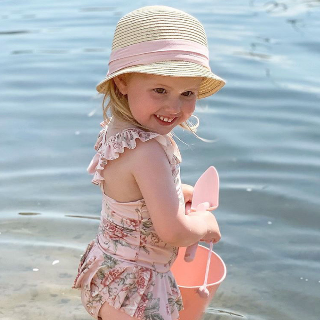 Little girl playing in the sea with scrunch silicone bucket and spade in old rose