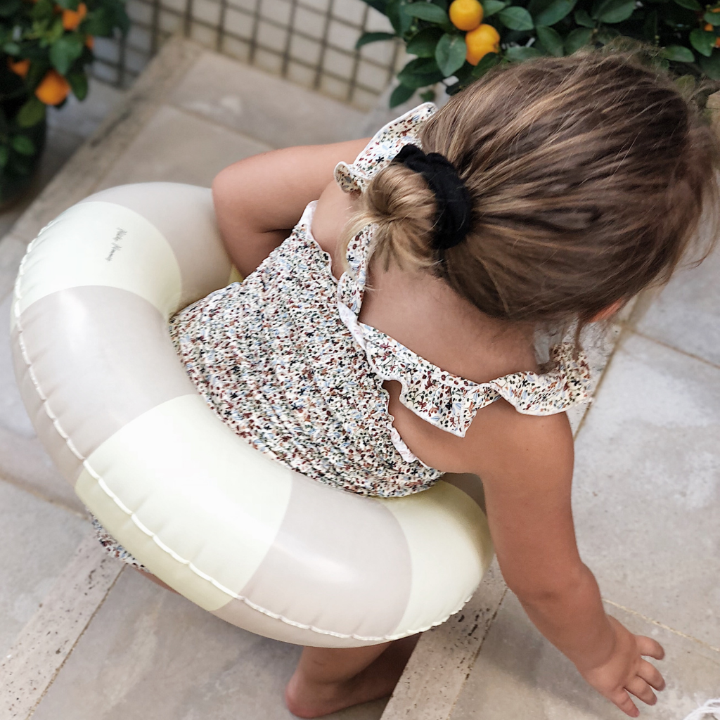 Little girl in floral swimsuit with Petites Pommes Emma grey inflatable rubber ring around her waist