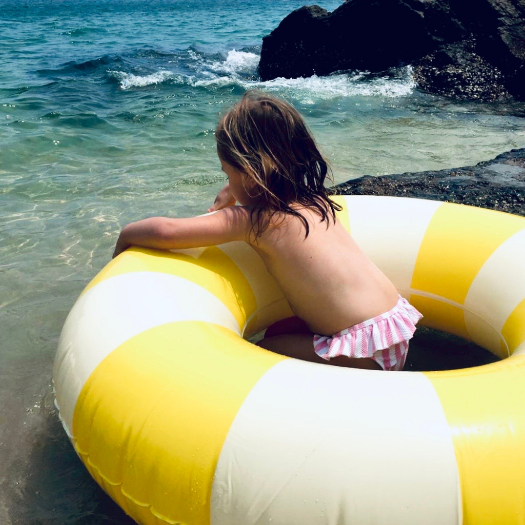 Little girl in the sea in her Petites Pommes Limonata yellow inflatable rubber ring