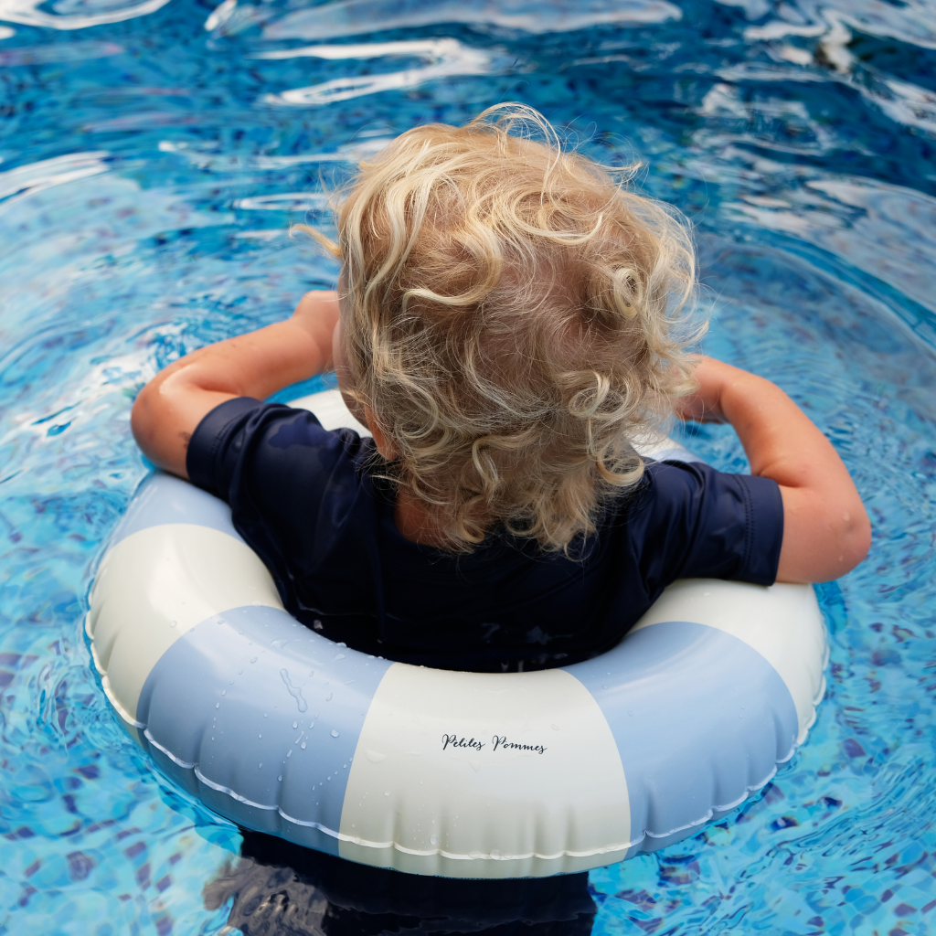 Little boy swimming in Petites Pommes inflatable rubber ring in Nordic Blue and white stripe
