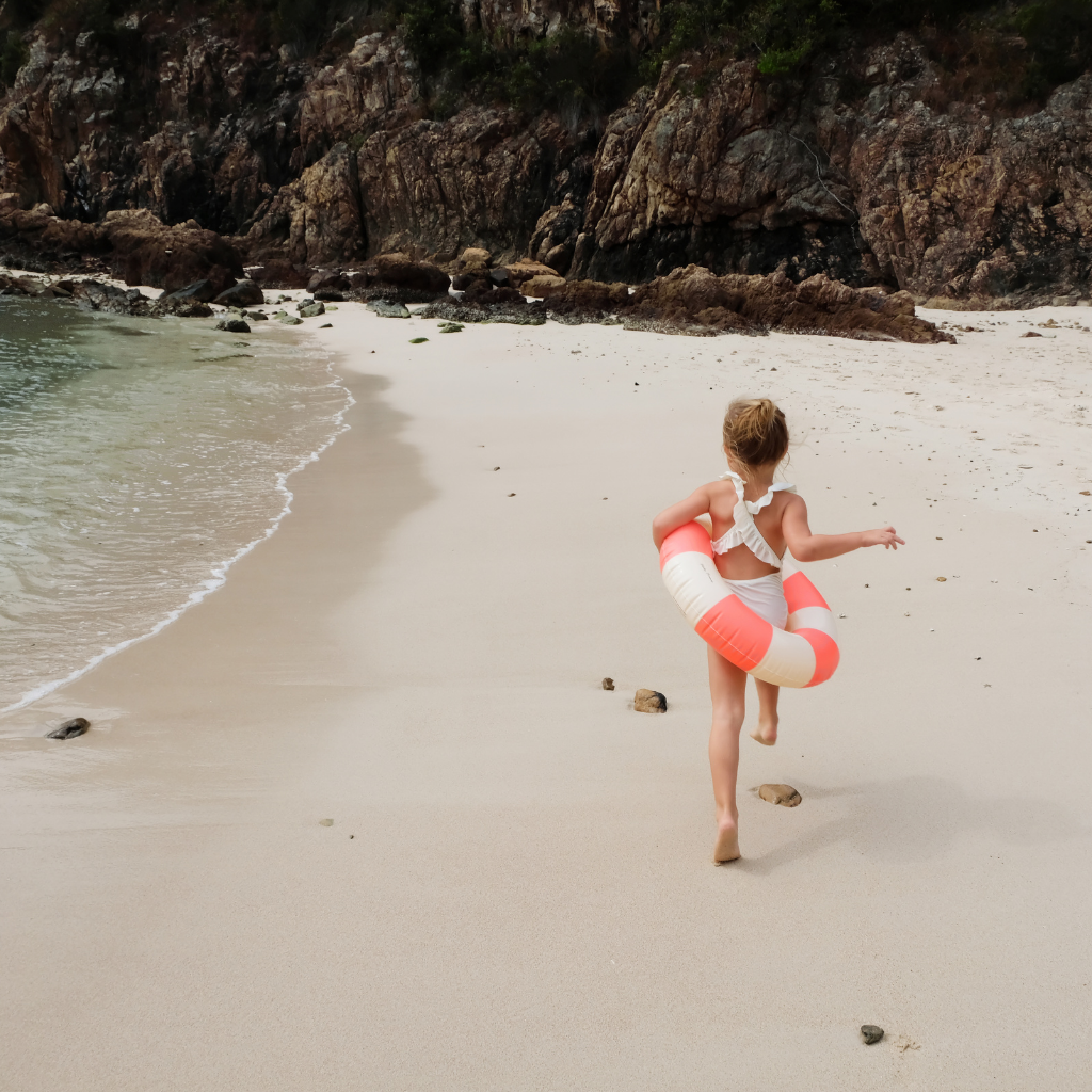 Little girl on the beach with Petites Pommes Sorbet Coral stripe rubber ring inflatable