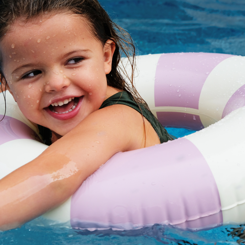 Little girl swimming in Petites Pommes rubber ring striped inflatable in violet purple