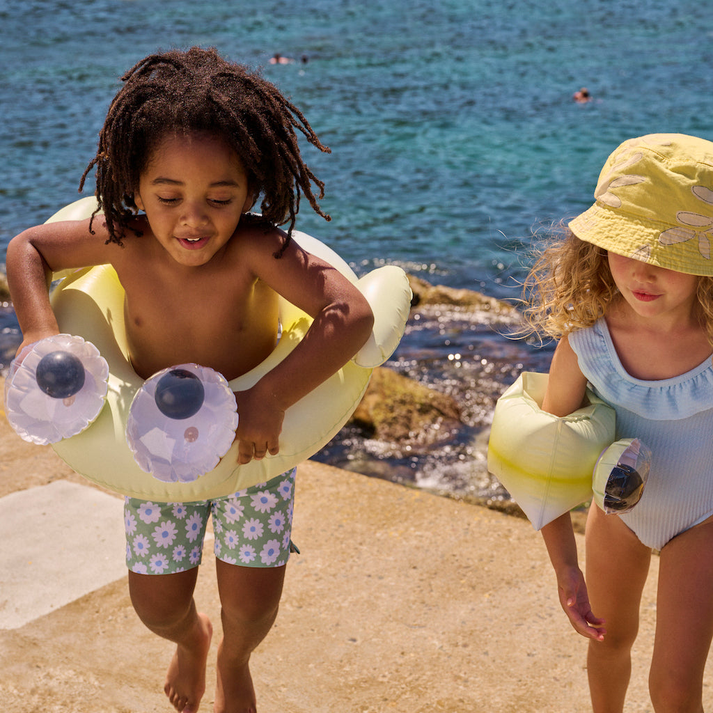 Two children by the sea wearing swim aids from Sunnylife including monty the Monster buddy float bands arm bands with 3d googly eyes 