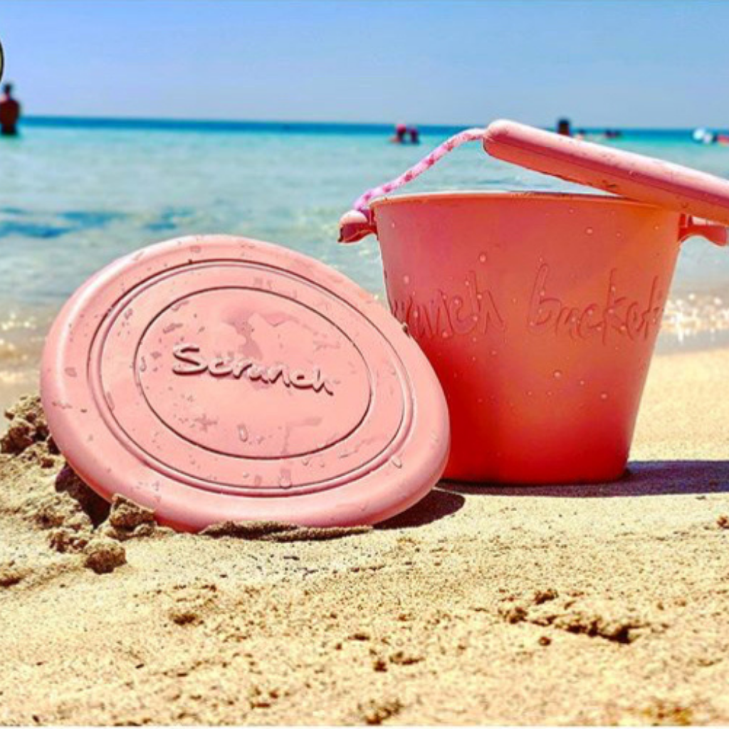 Scrunch silicone foldable frisbee flyer in old rose on the beach alongside a silicone bucket