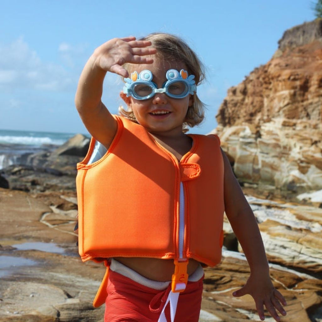 Little boy on the beach wearing Sunnylife Kids mini swim goggles in sonny the sea creature neon orange