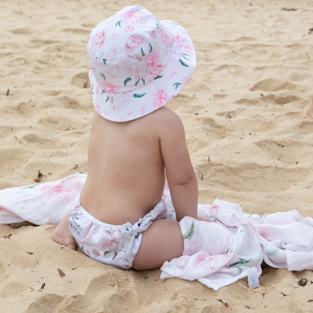 Little girl on the beach wearing Anchor & Arrow Pretty Peony print unisex reusable swim nappy