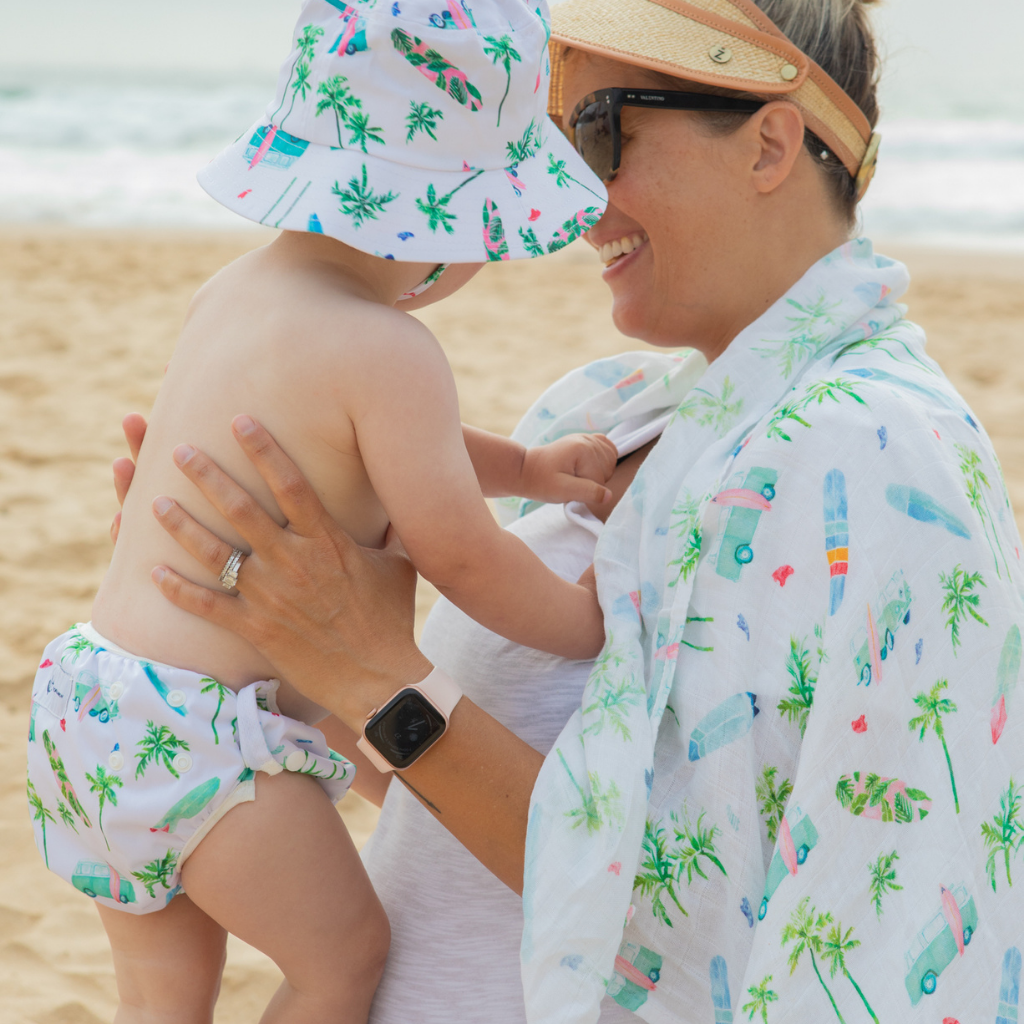 Baby with mummy on the beach wearing Anchor & Arrow Chasing Waves print unisex reusable swim nappy